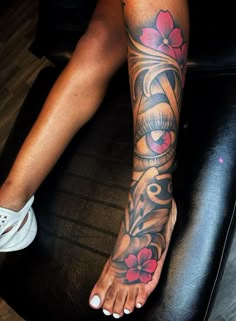 a woman's foot with tattoos on it sitting on a black leather chair in front of a wooden floor