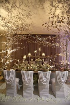 the table is set up with white chairs and centerpieces on top of it