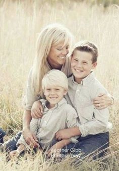 a woman and two boys are sitting in the tall grass with their arms around each other