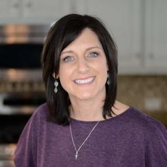 a woman standing in front of a stove top oven wearing a purple shirt and earrings