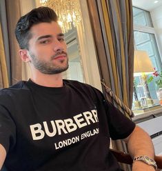 a man sitting in a chair wearing a burber london england t - shirt and looking off into the distance