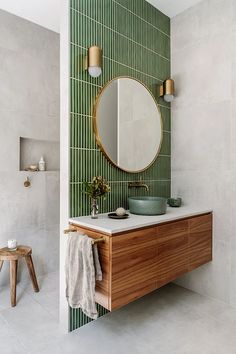 a bathroom with green tiles and a wooden sink vanity in front of a round mirror