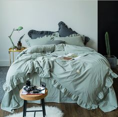 a bed with green sheets and pillows in a white room next to a lamp on a table