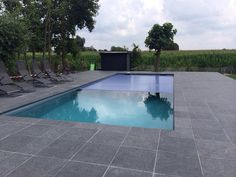 an empty swimming pool with lounge chairs around it and trees in the background on a cloudy day