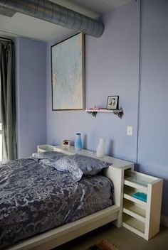 a bedroom with blue walls and a bed in the middle, next to a window