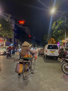 a person on a bike with a basket full of fruit in the street at night