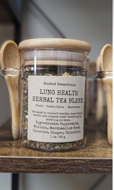 a jar filled with herbs sitting on top of a wooden table next to two spoons