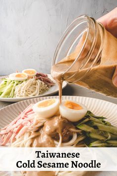 someone pouring sauce on a plate with noodles and vegetables