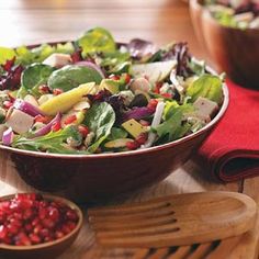 a salad in a bowl with apples and cranberries next to it on a wooden table