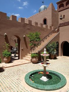 a fountain in the middle of a courtyard with stairs leading up to it and potted plants on either side