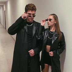 a man and woman standing next to each other in an empty hallway wearing black clothing