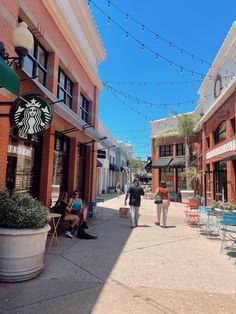 people are walking down the sidewalk in front of starbucks shops and restaurants on a sunny day