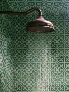 a shower head with water flowing from it in a green and white tiled bathroom area