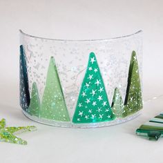 three small christmas trees in a clear glass container with confetti on the side