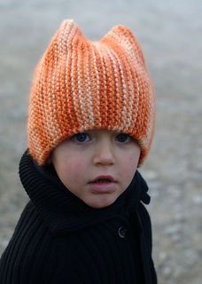 a young boy wearing an orange knitted hat and black coat, looking at the camera