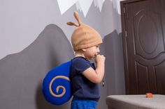 a little boy with a backpack and hat on is standing in front of a wall