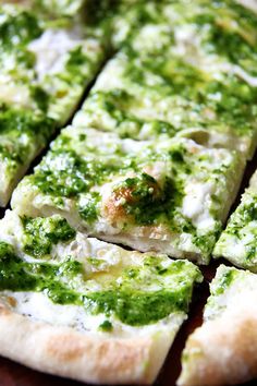 a pizza with cheese and pesto on it is cut into eight pieces, sitting on a wooden table