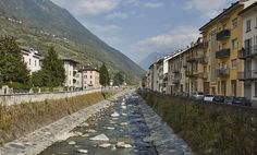 a river running through a city next to tall buildings and mountains in the back ground