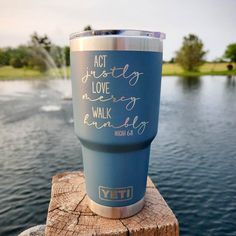 a blue yeti cup sitting on top of a wooden post next to a lake