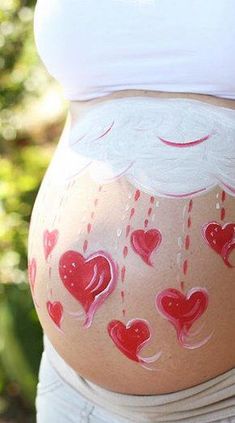 a pregnant woman with painted hearts on her stomach and belly is seen from the waist down