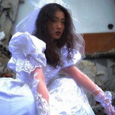 a woman in a white wedding dress is sitting on the ground with her hands out