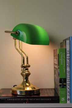 a green lamp sitting on top of a book shelf next to a stack of books