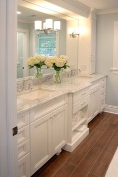 a white bathroom with two sinks and vases on the counter in front of it