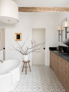 a bathroom with a large white tub and wooden cabinets in the corner, along with a vase filled with branches