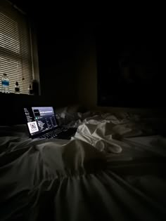 an open laptop computer sitting on top of a bed in a dark room next to a window