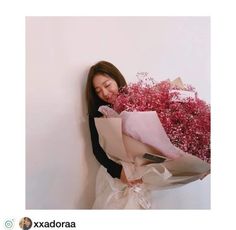 a woman is holding flowers and leaning against a wall with her face close to the wall