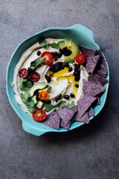 a bowl filled with hummus, olives and tomatoes next to tortilla chips