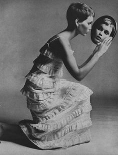 an old photo of a woman in a dress holding a mirror with her face on it