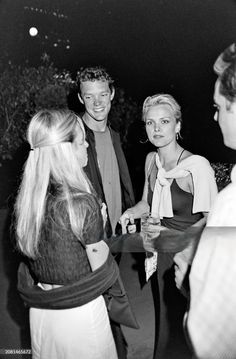 a group of people standing around each other in a black and white photo, talking