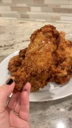 a person holding up a piece of fried chicken on a white plate in front of a marble counter top