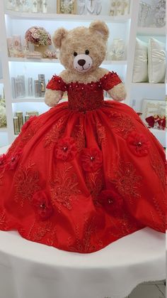 a teddy bear in a red dress sitting on a white table next to a shelf