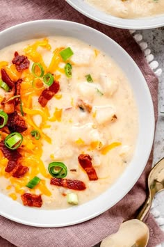 two bowls of soup with bacon, cheese and green onions on the side next to spoons