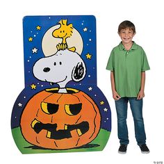 a young boy standing next to a cardboard cutout of snoopy on top of a pumpkin