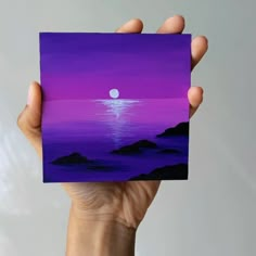 a hand holding up a purple and blue card with a full moon in the background