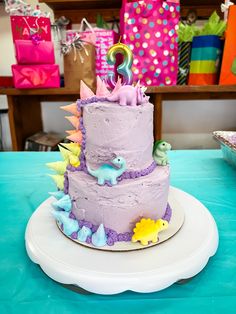 a birthday cake decorated with dinosaurs on a table in front of colorful boxes and presents