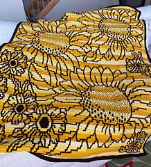 a crocheted yellow blanket with black and white designs on it, sitting on a bed