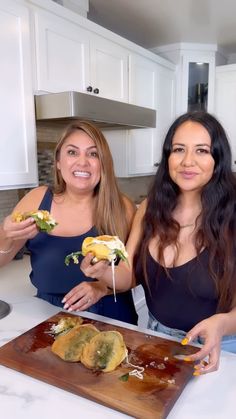 two women standing in front of a cutting board with food on it and one holding a knife