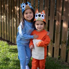 two young children dressed in costumes standing next to each other on the grass near a fence