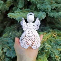 a hand holding a crocheted angel ornament in front of a pine tree