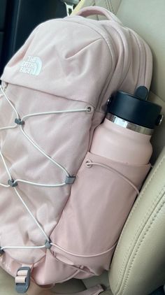 a pink backpack sitting in the back seat of a car next to a water bottle