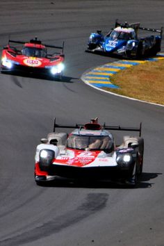 three race cars racing on a track with one driving behind the other, in motion