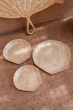 three white plates sitting on top of a floor next to a wicker chair