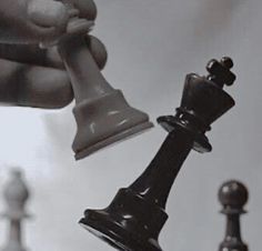 a hand holding a black and white chess piece over the other one's head