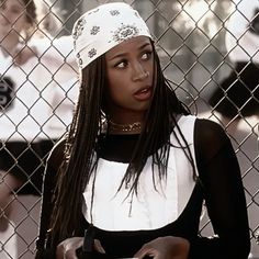 a woman with dreadlocks standing in front of a chain link fence holding a cell phone