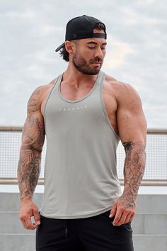 a man with long hair and tattoos on his arm, wearing a gray tank top