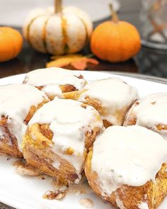 cinnamon rolls with icing on a white plate next to oranges and pumpkins